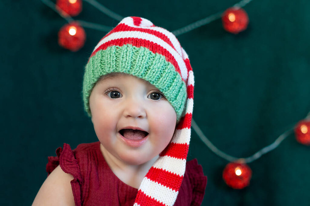 Carino bambino eccitato indossa cappello di Natale su decorato per il nuovo anno sfondo verde scuro. Primo Natale e Natale concetto di vendita. - Foto, immagini