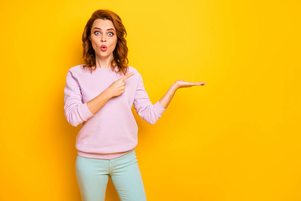 Photo of funny pretty lady open mouth hold novelty indicate finger product arm sale low prices shopping wear pink pullover green trousers isolated yellow color background - 写真・画像