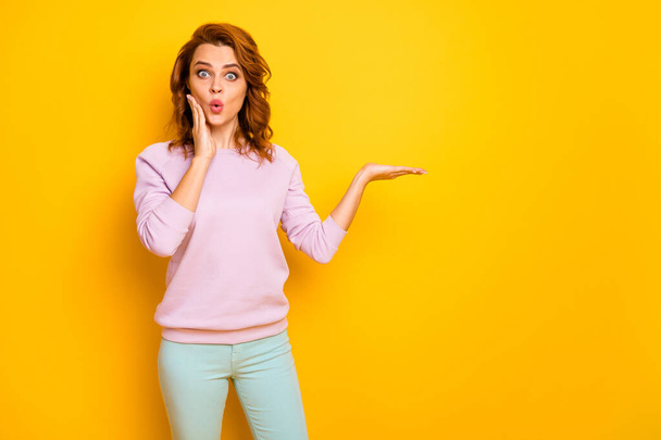 Photo of funny curly lady raise novelty product on open palm crazy breaking news black friday prices wear casual pink pullover green trousers isolated yellow color background - 写真・画像