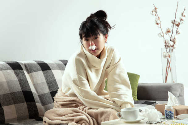 Woman wrapped in a plaid looks sick, ill, sneezing and coughing sitting at home indoors - Photo, image