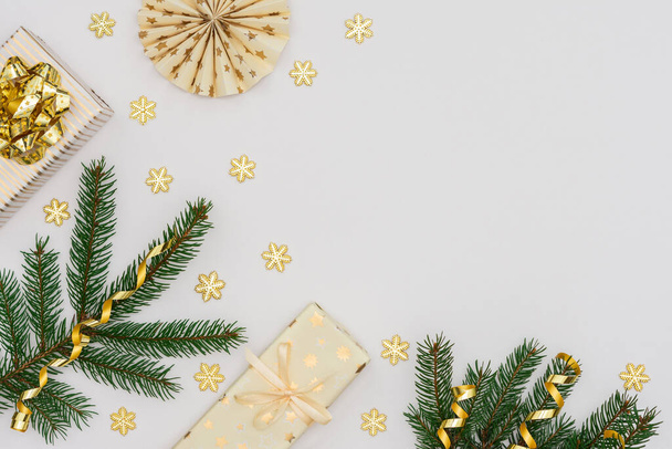Fondo festivo con decoración de oro, ramas de abeto verde y cajas de regalo de oro con arco, copos de nieve brillantes y decoraciones de árboles de navidad de papel, planas, vista superior - Foto, imagen