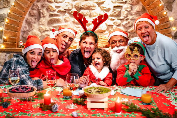 クリスマスフェスティバルハウスパーティーで楽しいサンタの帽子を持つ多世代の大家族の面白い自撮り写真-壮大な両親と子供たちと一緒に食べる冬の休日のクリスマスのコンセプト-鮮やかなフィルター - 写真・画像