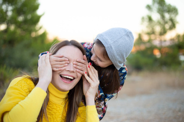 Felice giovane ragazza ridendo, coprendo gli occhi di sua madre con la mano. - Foto, immagini