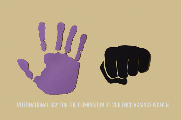 de tekst van de internationale dag voor de uitbanning van geweld tegen vrouwen en een open hand uitgesneden in een violette krant en een vuist, die het geweld weergeeft, op een beige achtergrond - Foto, afbeelding