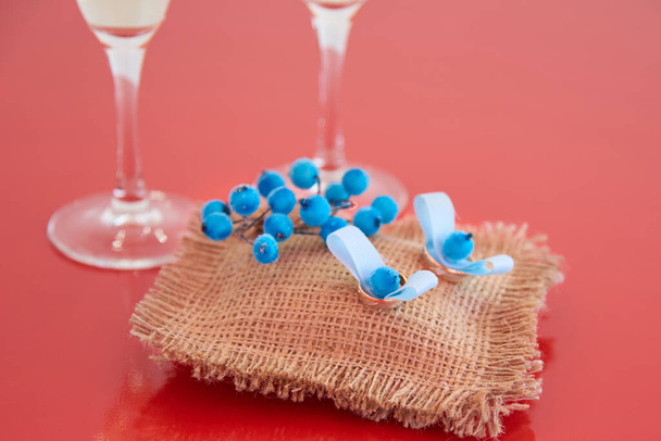 Goldringe für die Hochzeit auf Leinenstoff ausgelegt und mit blauen Beeren auf rotem Hintergrund verziert - Foto, Bild