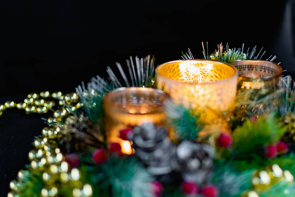 Christmas decorations on a black background by candlelight. Composition of Golden balls and beads, openwork candlesticks with patterns and branches of the Christmas tree. Elegant cones and red berries in the festive presentation - Photo, Image