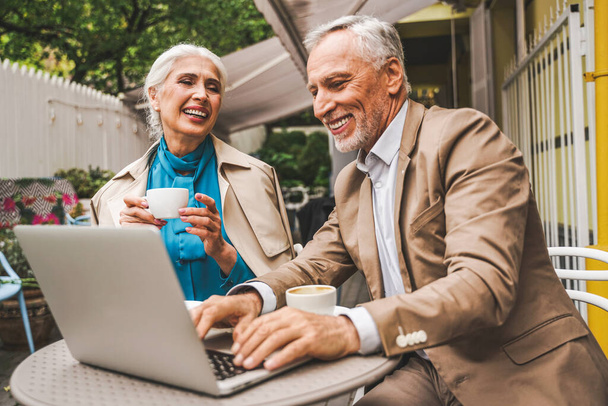 Beautiful senior couple dating outdoors - Mature couple with laptop computer sitting in a bar restaurant, concepts about elderly, lifestyle and technology - Foto, immagini