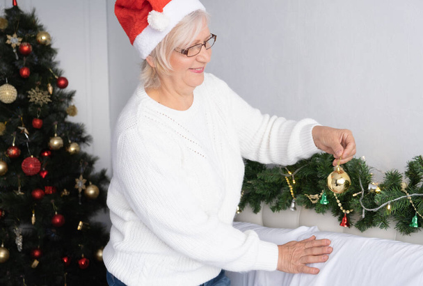 Mujer senior positiva decorando la habitación para Navidad. estilo de vida interior, concepto de vejez. - Foto, imagen
