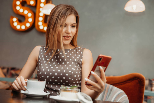 Mooie ontspannen vrouw met behulp van een mobiele telefoon in cafe. Nieuws of SMS lezen - Foto, afbeelding