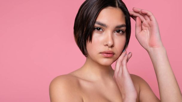 Close up face of beautiful young woman with clean perfect skin. Portrait of beauty model with natural nude make up. Spa, skin care and wellness. Pink peach coral background. 16:9 panoramic format. - Foto, Imagem