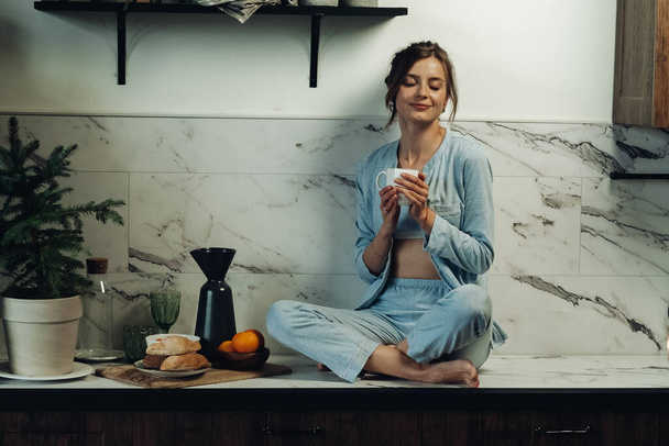 Delighted lady with cup in hands enjoying morning in kitchen - Фото, зображення