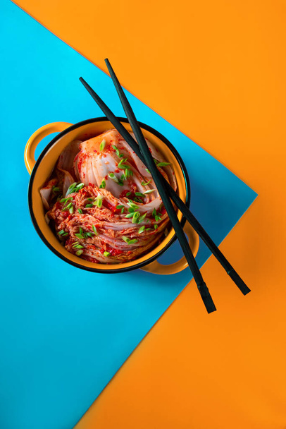 Kimchi cabbage in a bowl with chopsticks on a colored background, top view, Korean cuisine. Trend food photography - Photo, Image