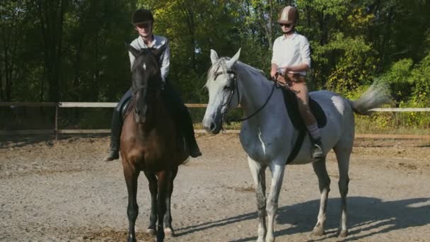 Kaksi naispuolista ratsastajaa ratsastusvaatteissa ja kypärissä poistuivat hevosistaan. - Materiaali, video