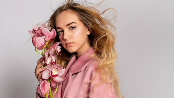 Seductive blonde woman in pink jacket posing in studio on grey background. elegant model in pastel casual spring outfit. Beautiful girl with healthy skin and branch orchid. 16:9 panoramic format. - Фото, зображення