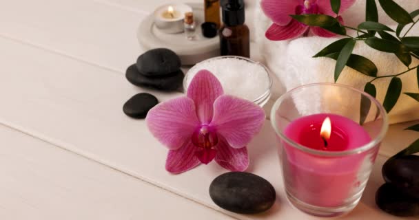 accesorios de spa y bienestar - vela encendida con sal de baño, piedras de masaje y aceites sobre mesa de madera - Imágenes, Vídeo