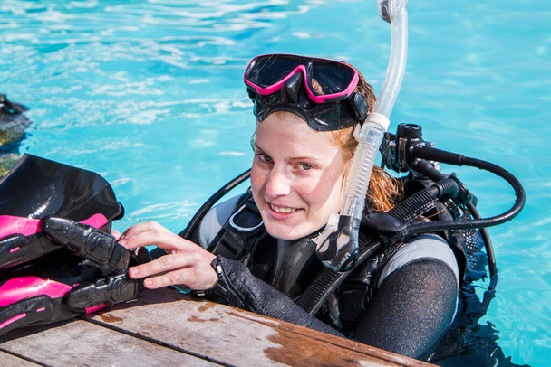 Scuba dive training in a pool, diver looking at the camera putting her fins on the deck smiling. - Photo, Image
