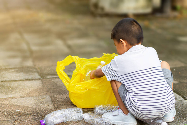 В городском общественном парке. Азиатский мальчик доброволец для уборки полей. Он подбирает много пластиковой бутылки и соломы на земле. Экономия окружающей среды и сокращение отходов. - Фото, изображение