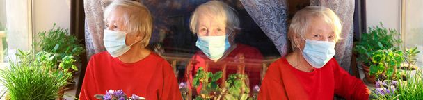 Koncepcja Covid-19, zdrowie, bezpieczeństwo i pandemia - starsza samotna kobieta nosząca ochronną maskę medyczną siedząca w pobliżu okna w domu dla ochrony przed wirusem - Zdjęcie, obraz
