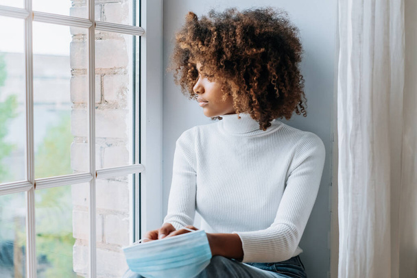Mujer joven pensativo sentado en el alféizar de la ventana blanca moderna - Foto, imagen