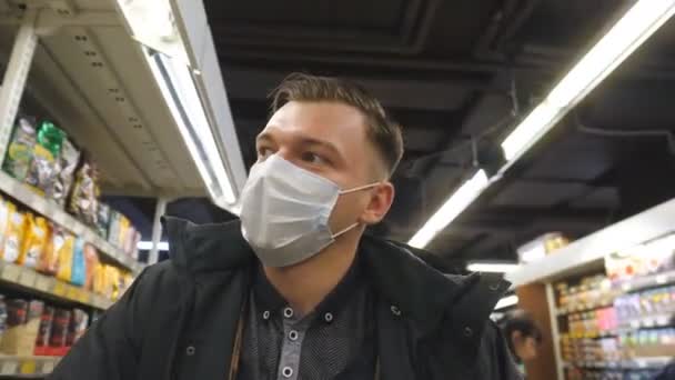 Egy arcmaszkos fiatalember portréja, aki a szupermarketben sétál. Egy fickó, aki védőmaszkot visel a vírustól. Bevásárlás a boltban a koronavírus világjárvány idején. Az egészség fogalma. COVID-19 szám - Felvétel, videó