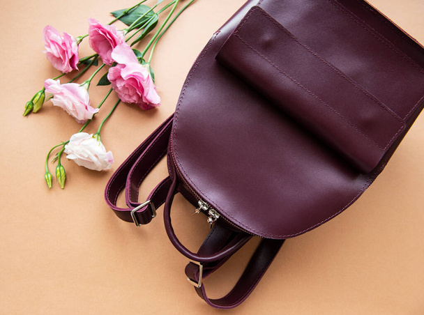 Женский кожаный рюкзак и цветы на светлом коричневом фоне - Фото, изображение