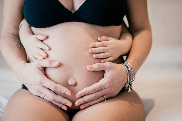 Close up picture of pregnant woman and her baby holding her belly - Baby holding the belly of his pregnant mother - Pregnant woman and her baby holding hands together - Love for family, parenting - Фото, зображення