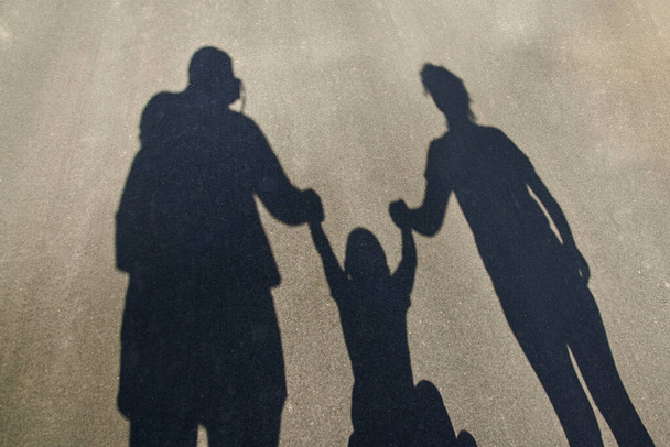 Silueta, sombra de una familia en el pavimento: papá, mamá y bebé tomados de la mano. - Foto, Imagen