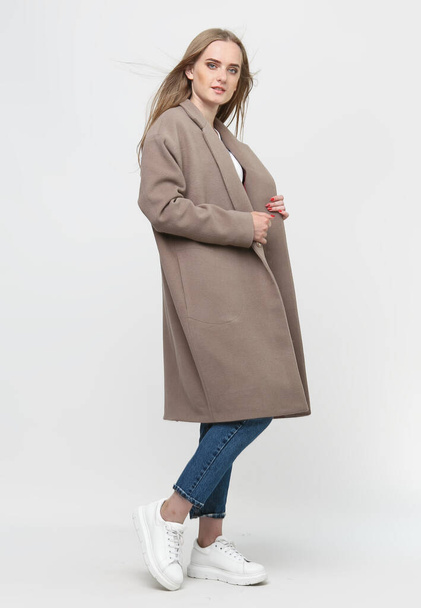 hermosa modelo posando en un abrigo largo marrón sobre un fondo blanco. Grabado en estudio. Concepto de publicidad de ropa. - Foto, imagen