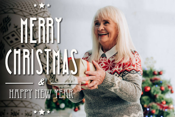 ενθουσιασμένοι ηλικιωμένη γυναίκα παρουσιάζει δώρο στον σύζυγο κοντά χαρούμενα Χριστούγεννα και χαρούμενη γραμματοσειρά του νέου έτους   - Φωτογραφία, εικόνα