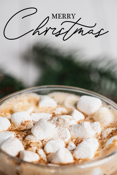 Close up view of glass cup of cocoa with marshmallows and cinnamon near merry christmas lettering  - Фото, изображение