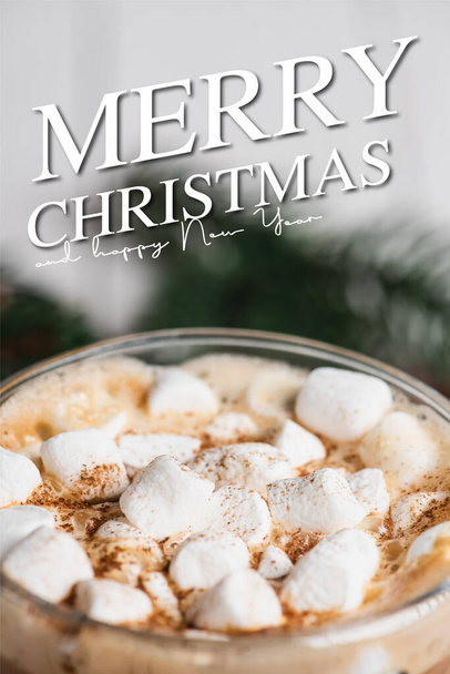 Close up view of glass cup of cocoa with marshmallows and cinnamon near merry christmas and happy new year lettering  - Photo, Image