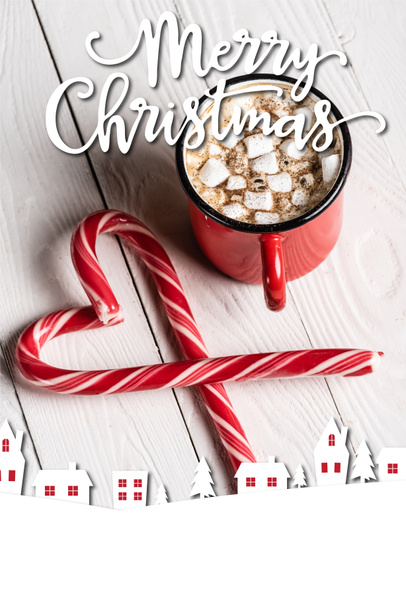 Red cup of cocoa near christmas candy canes near merry christmas lettering on wooden background - Zdjęcie, obraz