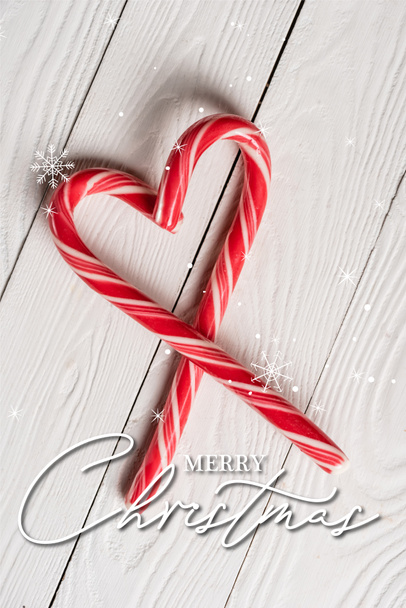 木の背景に陽気なクリスマスのレタリングの近くの心の形で甘いキャンディーの杖のトップビュー - 写真・画像