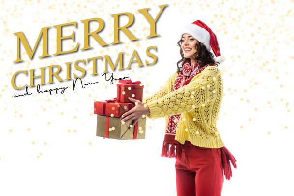 Радостная молодая женщина в шапке Санты, шарфе и вязаном свитере с подарками рядом с Рождеством и счастливым новым годом с надписью на белом - Фото, изображение