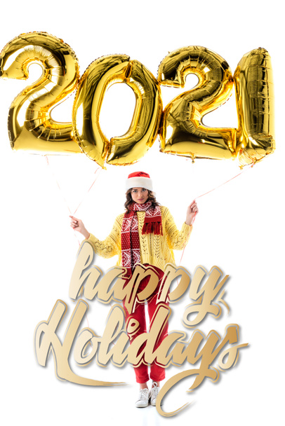 young woman in santa hat and scarf holding balloons with 2021 numbers near happy holidays lettering on white - Photo, Image