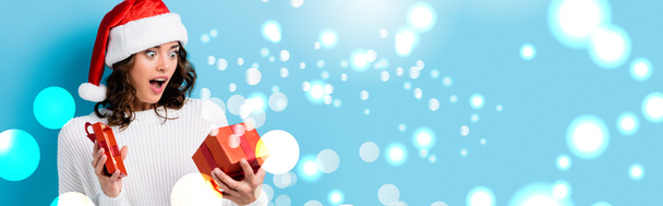 young shocked woman looking at gift box near snow illustration on blue, banner - Photo, Image