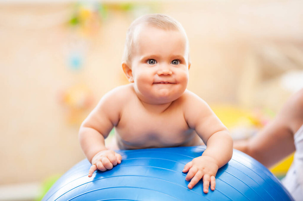 Smiling baby lying on big blue fitness ball at home. - Photo, image