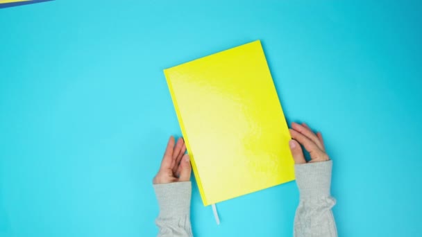 dvě ženské ruce otáčejí stránky žlutého zápisníku s prázdnými bílými listy na modrém pozadí, horní pohled - Záběry, video