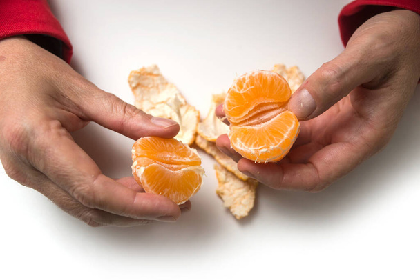 Closeup of hands of man peeling an organic tangerine on white background - Fotó, kép