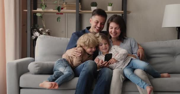 Happy family with little children using smartphone entertaining on internet - 映像、動画