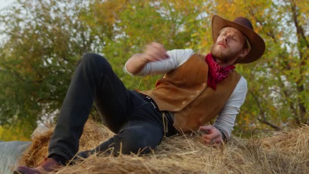 Komea cowboy poseeraa lähellä heinää maatilallaan - Materiaali, video