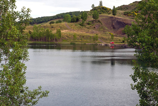 Lagune umgeben von Pappel- und Eichenwäldern mit einem roten Auto am Ufer. See in einem ehemaligen Tagebau entstanden  - Foto, Bild