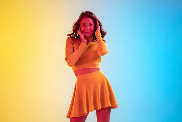 Beautiful seductive girl in fashionable, romantic yellow outfit on bright gradient yellow-blue background in neon light - Valokuva, kuva