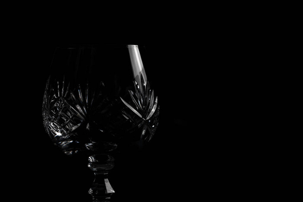 Empty crystal brandy glass on a dark black background in dramatic lighting. Isolated fine dining drinking glass bar & restaurant - Photo, Image