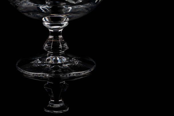Empty crystal brandy glass reflection of stand on a dark black background in dramatic lighting. Isolated fine dining drinking glass - Photo, Image
