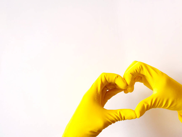 Yellow latex gloves make heart on white background. Concept support and disinfection, copyspace. - Foto, Bild