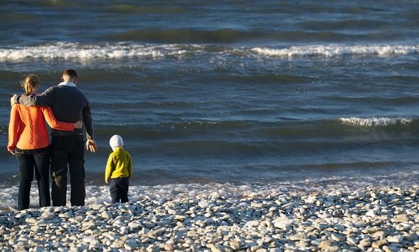 Famiglia di tre persone sulla spiaggia di ghiaia
 - Foto, immagini
