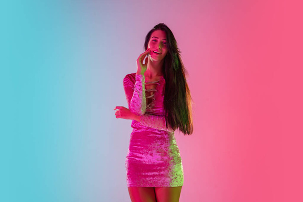 Beautiful seductive girl in fashionable dress, outfit on bright gradient pink-blue background in neon light - Fotografie, Obrázek