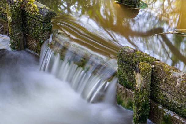 Ein kleiner Wasserfall, der durch einen Höhenunterschied in einem Bach im Park entsteht - Foto, Bild