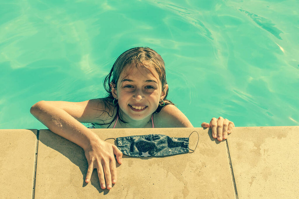 Yüzme havuzunda koruyucu maskeli genç bir kız. Coronavirus salgını kavramı 2020 yazında bir seyahat endüstrisi üzerinde etkili oldu. Kız havuzda koruyucu bir maske takarak yüzüyor. - Fotoğraf, Görsel